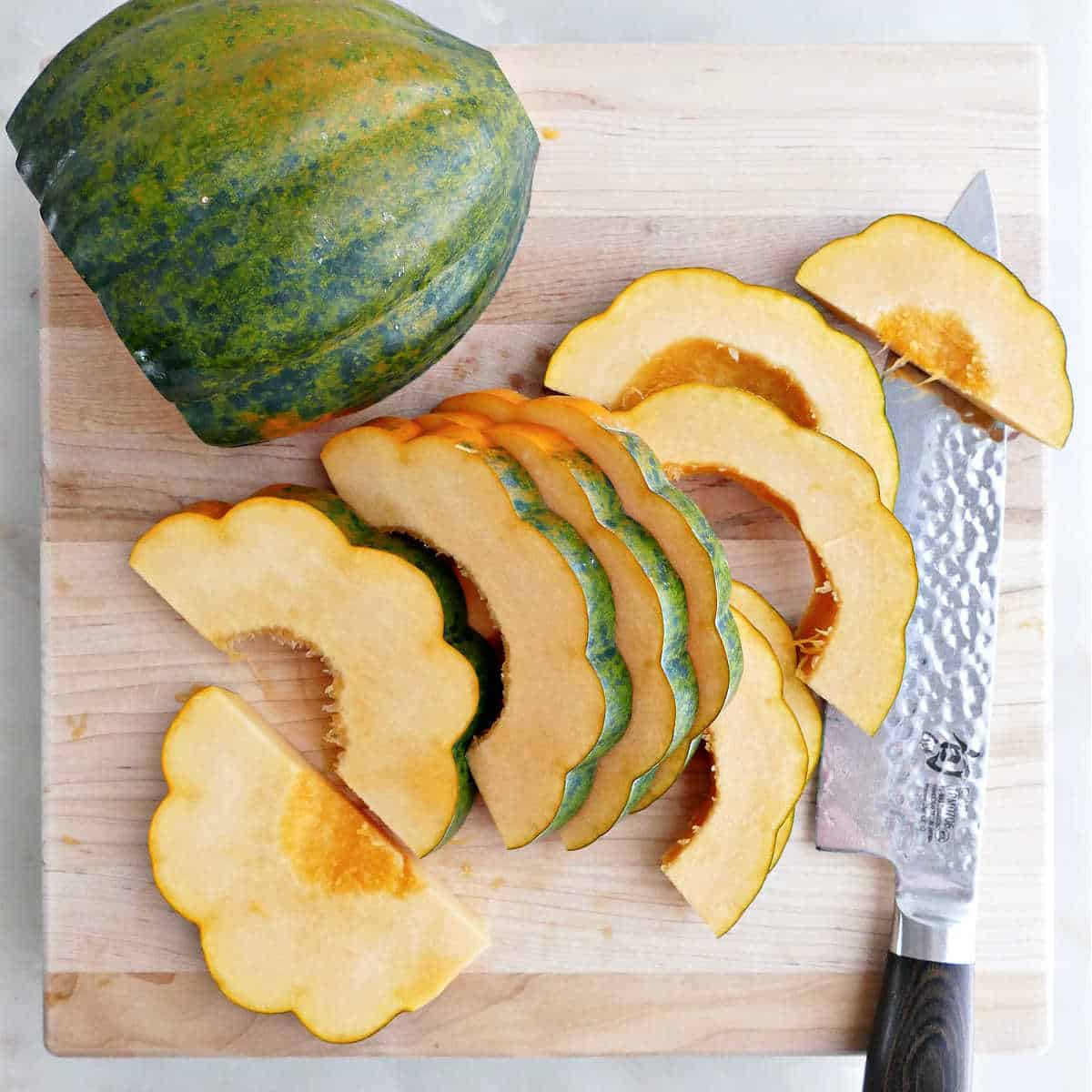 Acorn squash half cut into thin slices on a cutting board.
