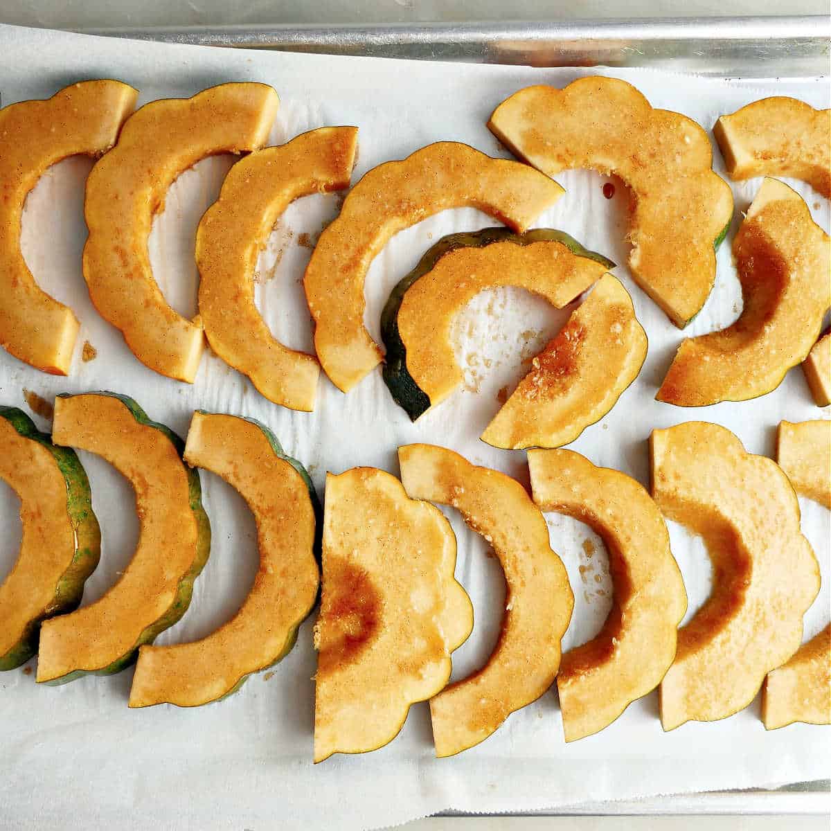 Acorn squash slices brushed with oil and seasonings on a lined baking sheet.