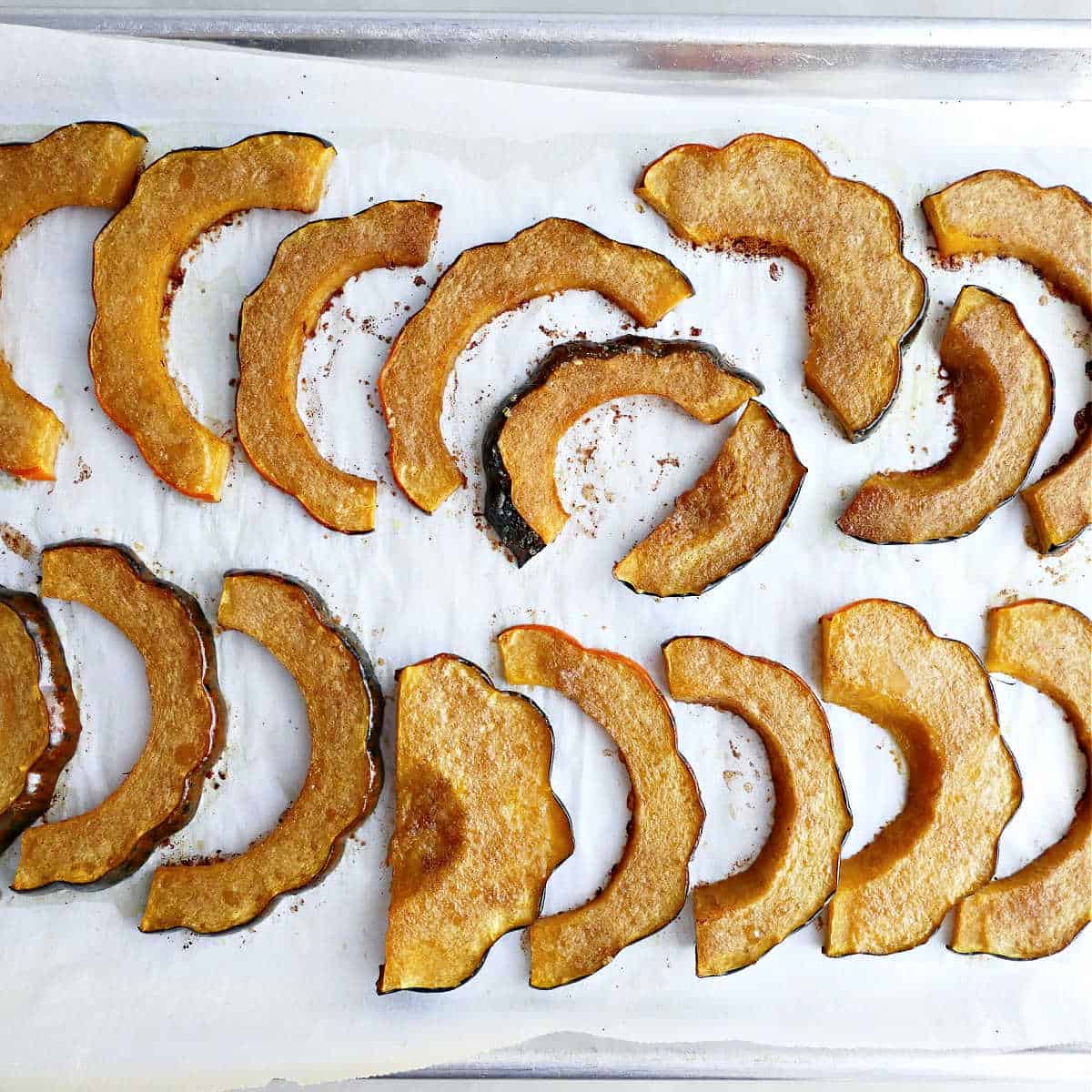 Roasted squash slices on a lined baking sheet after coming out of the oven.