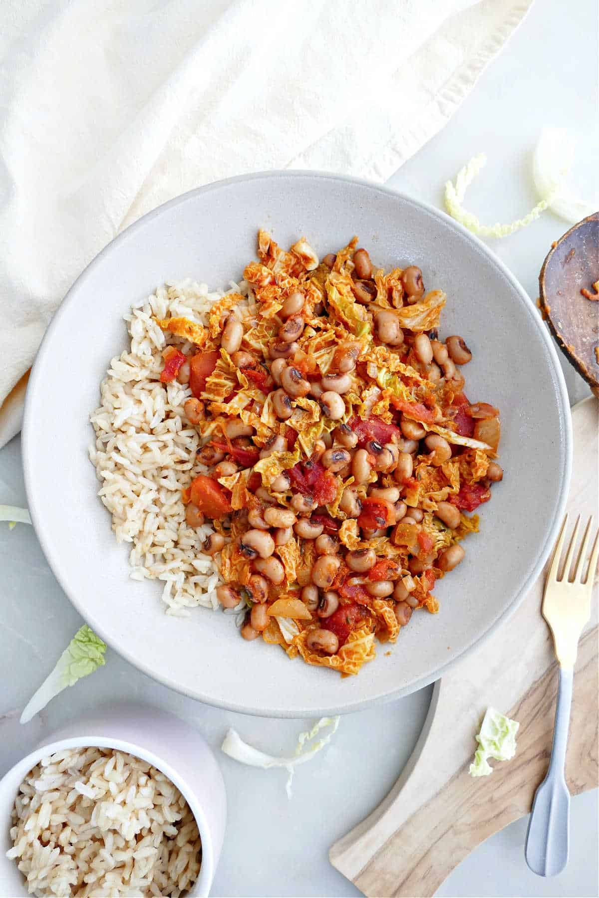 Black eyed pea and cabbage stew next to rice, a fork, and a napkin.