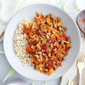 Black eyed pea and cabbage stew next to rice, a fork, and a napkin.