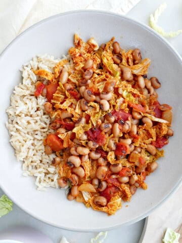 Black eyed pea and cabbage stew next to rice, a fork, and a napkin.