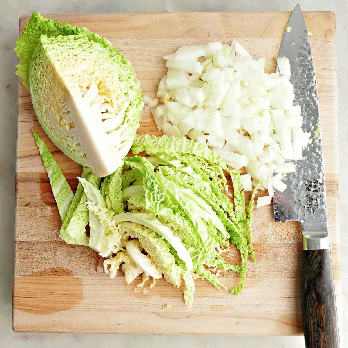 Cabbage and onion cut into pieces on a cutting board with a knife.