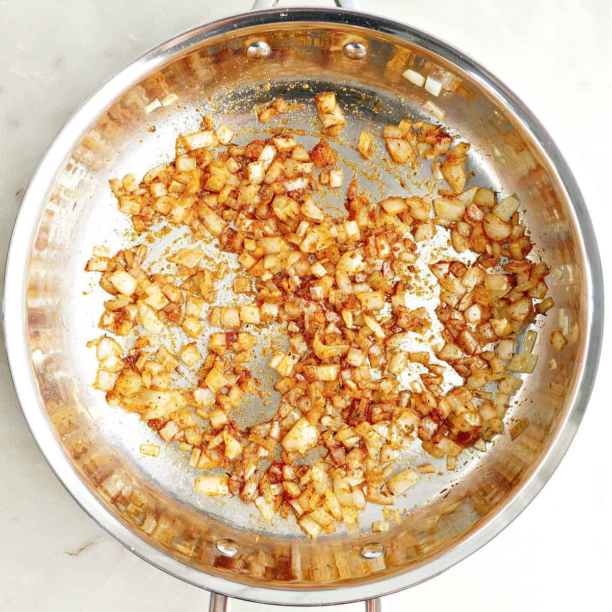 Onion cooking in olive oil and spices in a skillet.