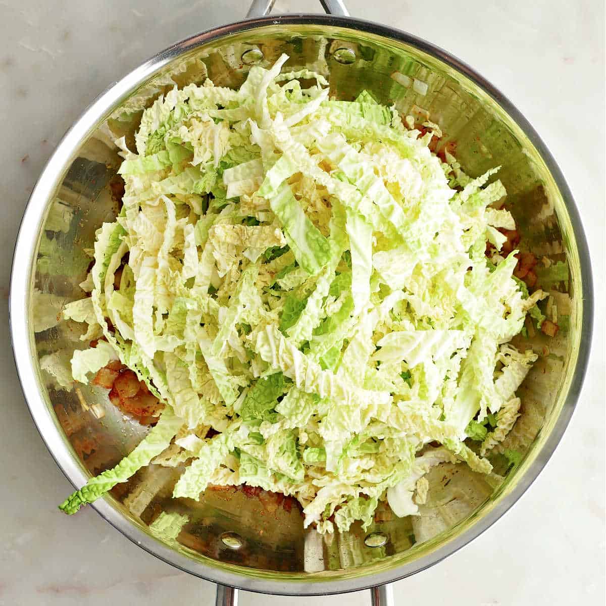 Shredded cabbage added to a skillet with onion and spices.