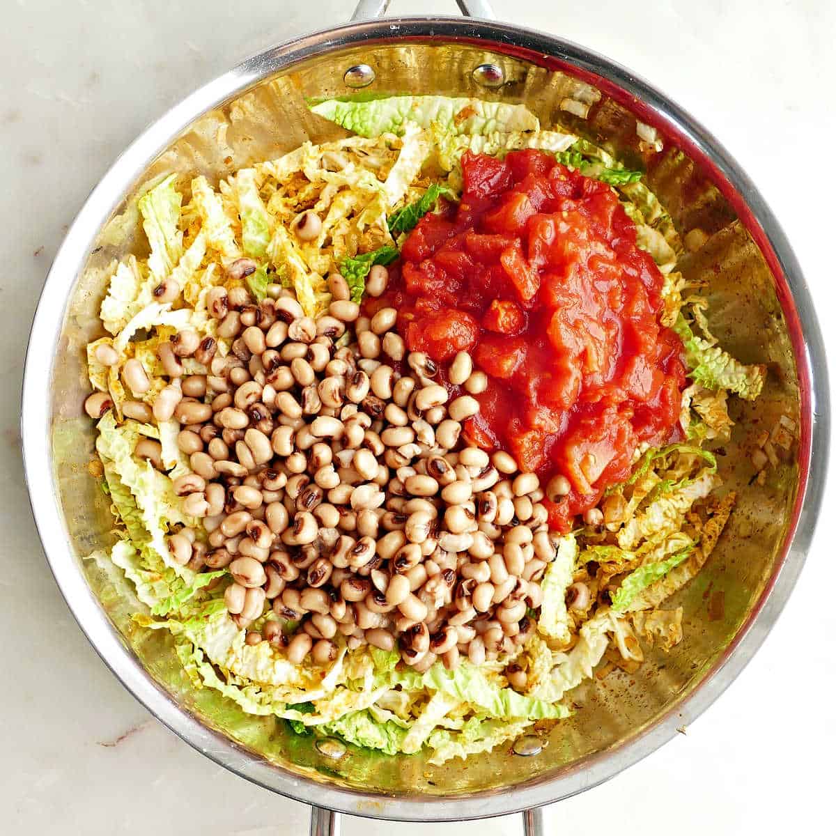 Black eyed peas, broth, and diced tomatoes being added to a skillet with cabbage.