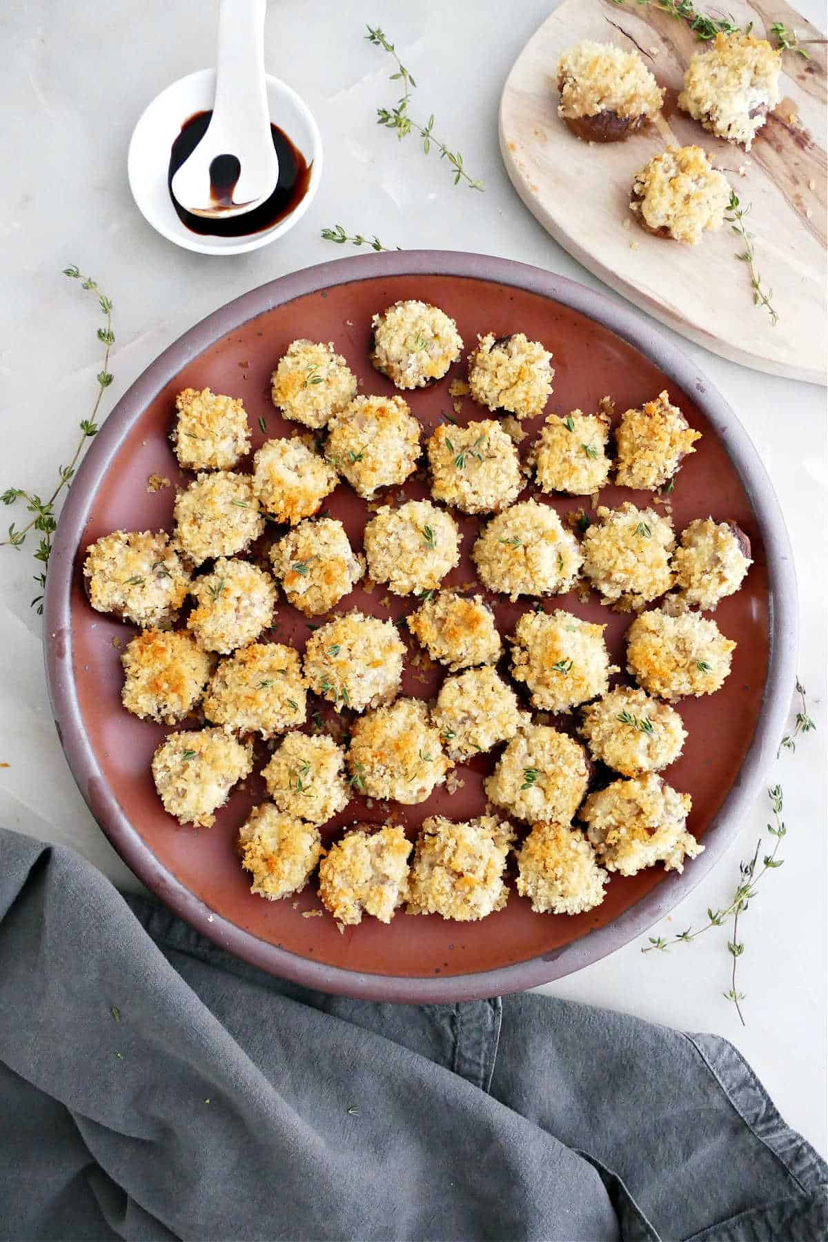 Boursin stuffed mushrooms on a plate next to garnishes, napkin, and wooden board.