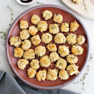 Boursin stuffed mushrooms on a plate next to garnishes, napkin, and wooden board.