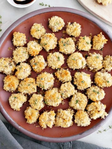 Boursin stuffed mushrooms on a plate next to garnishes, napkin, and wooden board.