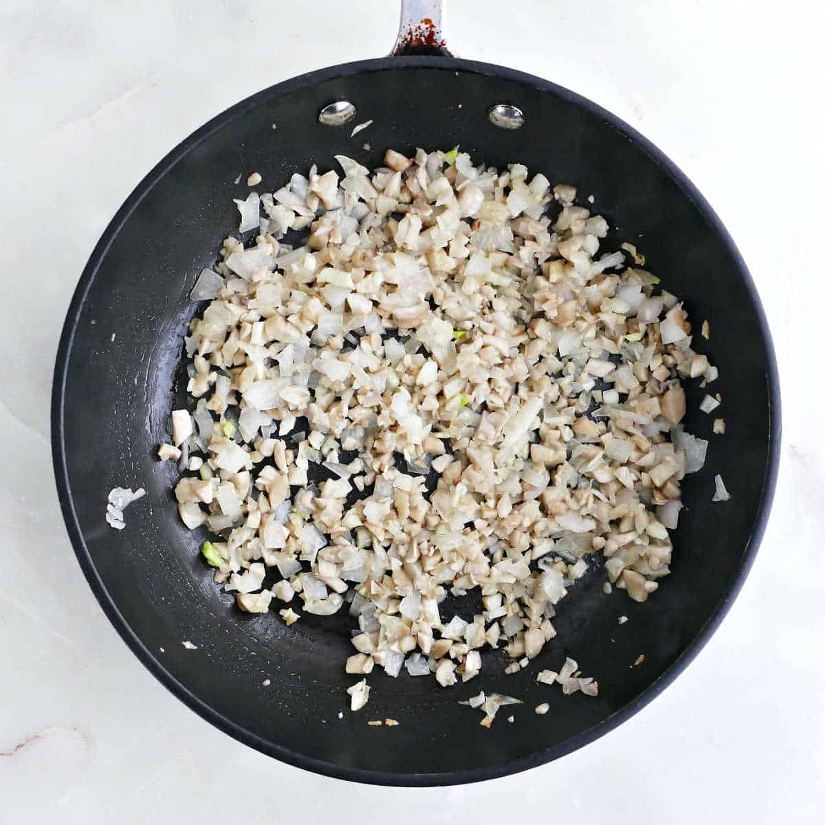 Shallots, garlic, and mushroom stems cooking in olive oil in a skillet.