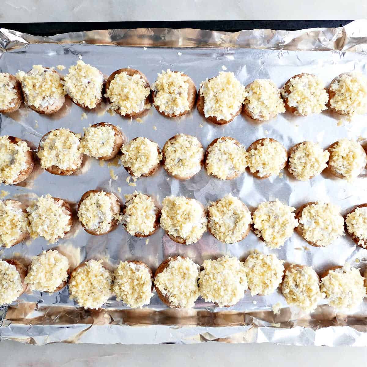 Stuffed mushrooms coated with breadcrumbs on a baking sheet before going into the oven.