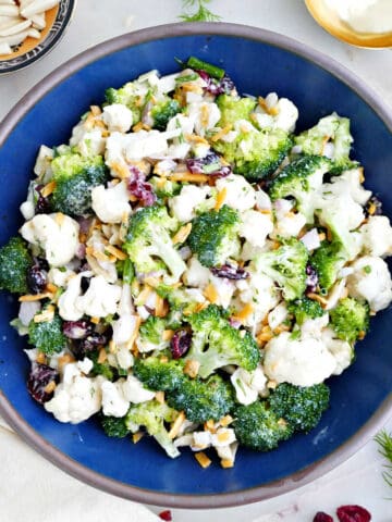 Broccoli and cauliflower salad in a bowl next to garnishes, a napkin, and a spoon.