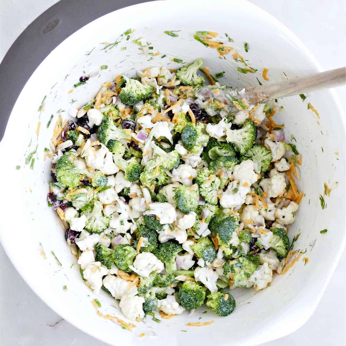 Broccoli and cauliflower salad recipe mixed together in a bowl with a spoon.