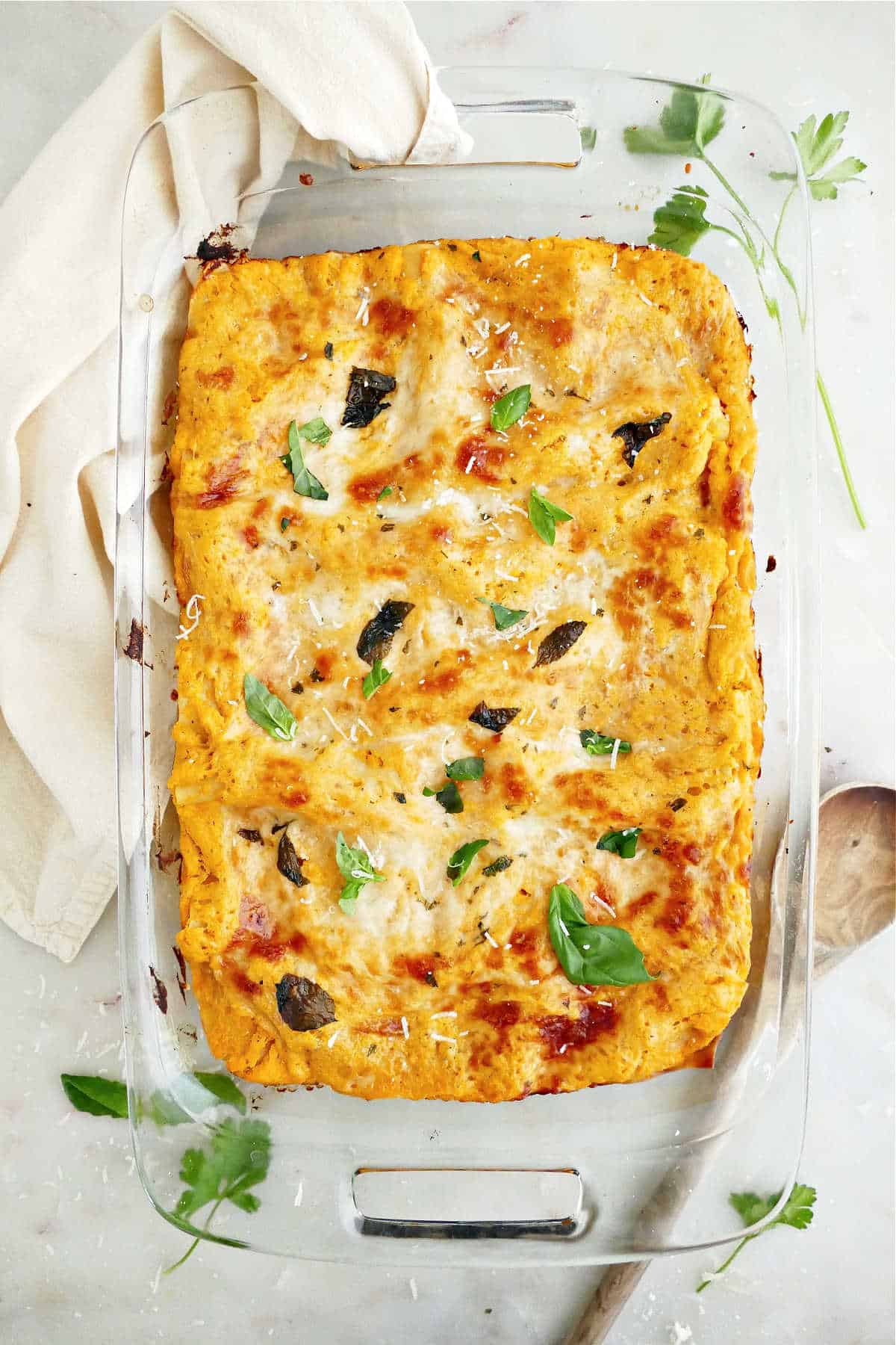 Butternut squash lasagna in a baking dish next to herbs, napkin, and spoon.