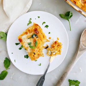 Slice of butternut squash lasagna on a plate with a fork next to tray of it.