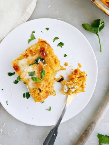 Slice of butternut squash lasagna on a plate with a fork next to tray of it.