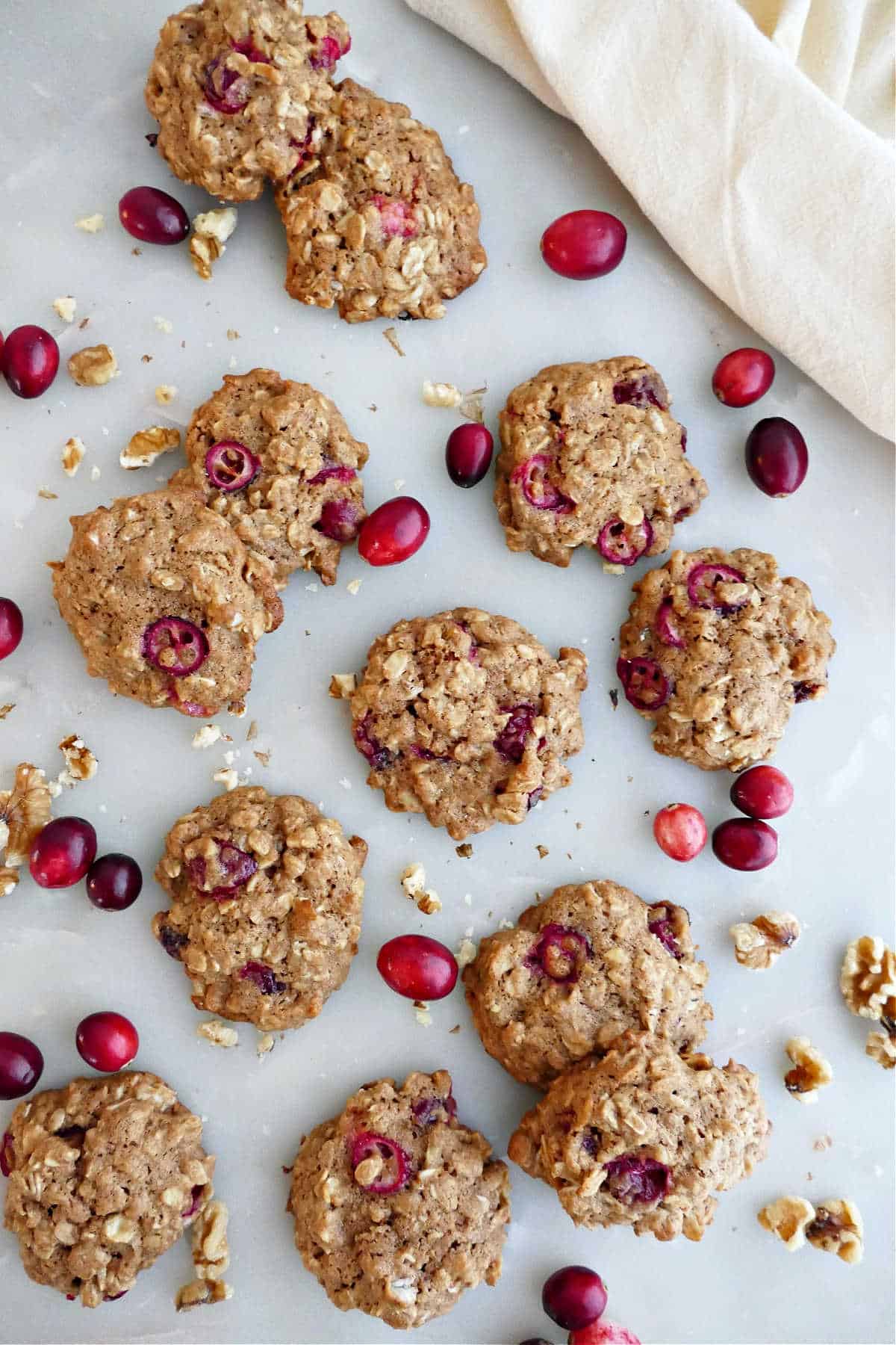 Twelve oatmeal cranberry walnut cookies on a counter surrounded by cranberries and walnuts.