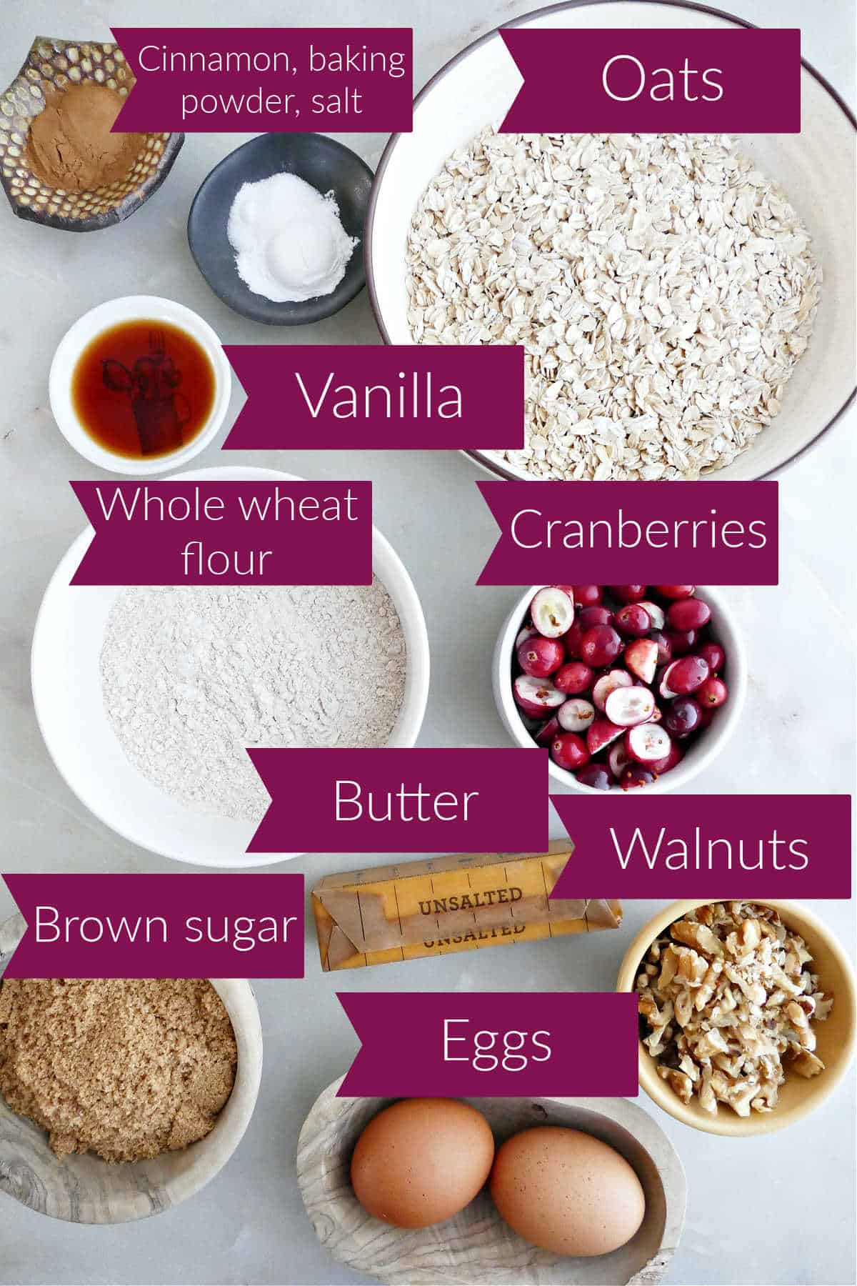 Spices, oats, vanilla, flour, cranberries, brown sugar, butter, walnuts, and eggs on a counter with labels.