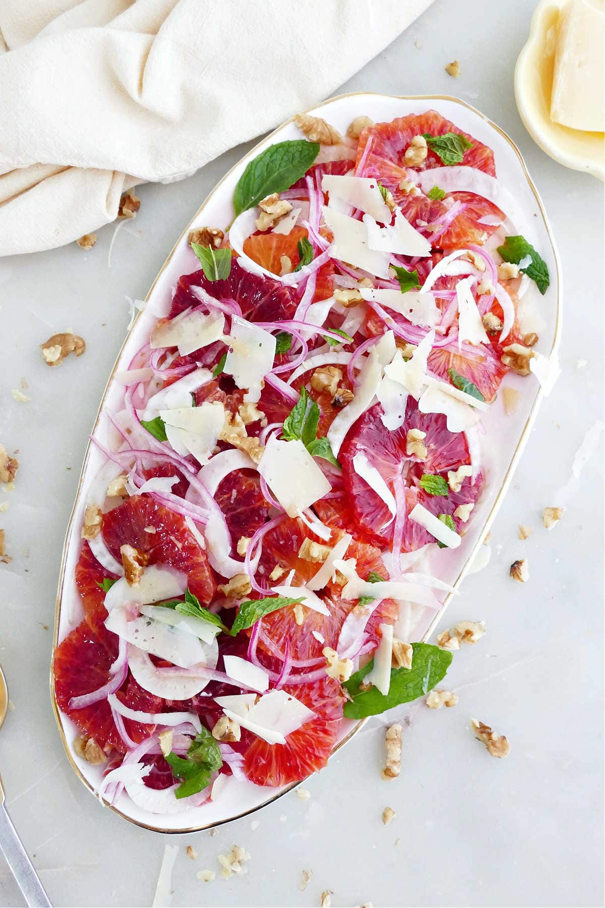 Blood orange fennel salad on an oval serving tray next to napkin and toppings.