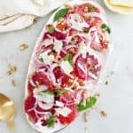 Blood orange fennel salad on an oval serving tray next to napkin and toppings.