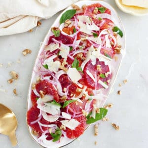 Blood orange fennel salad on an oval serving tray next to napkin and toppings.