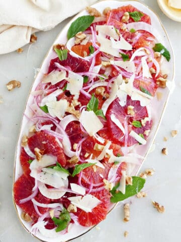 Blood orange fennel salad on an oval serving tray next to napkin and toppings.