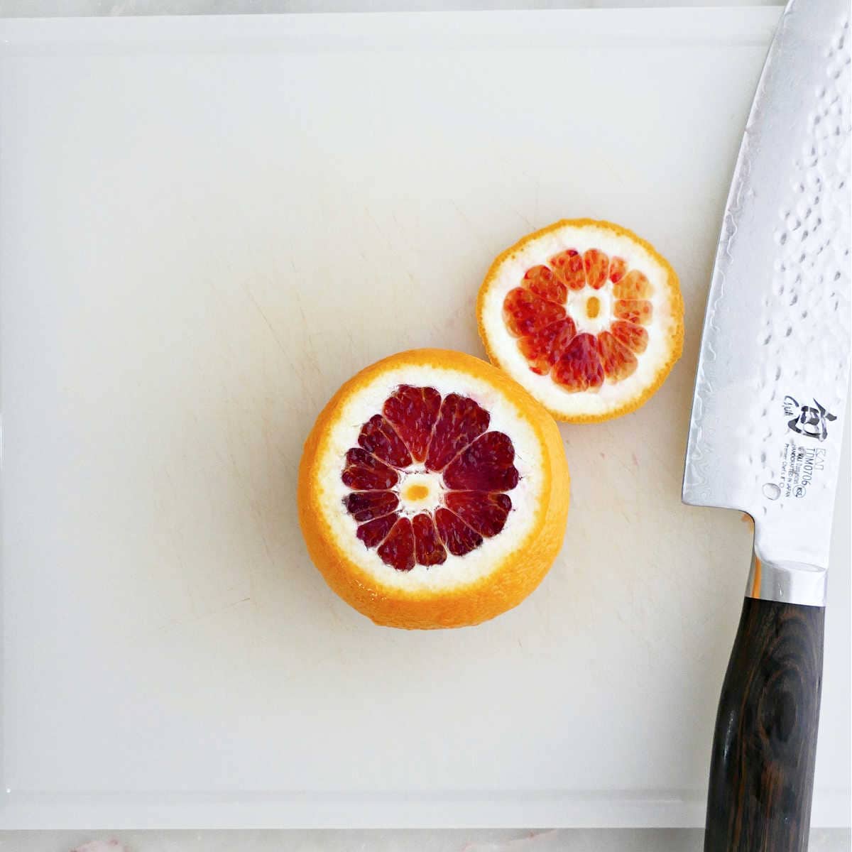 Blood orange with top trimmed off on a cutting board next to knife.