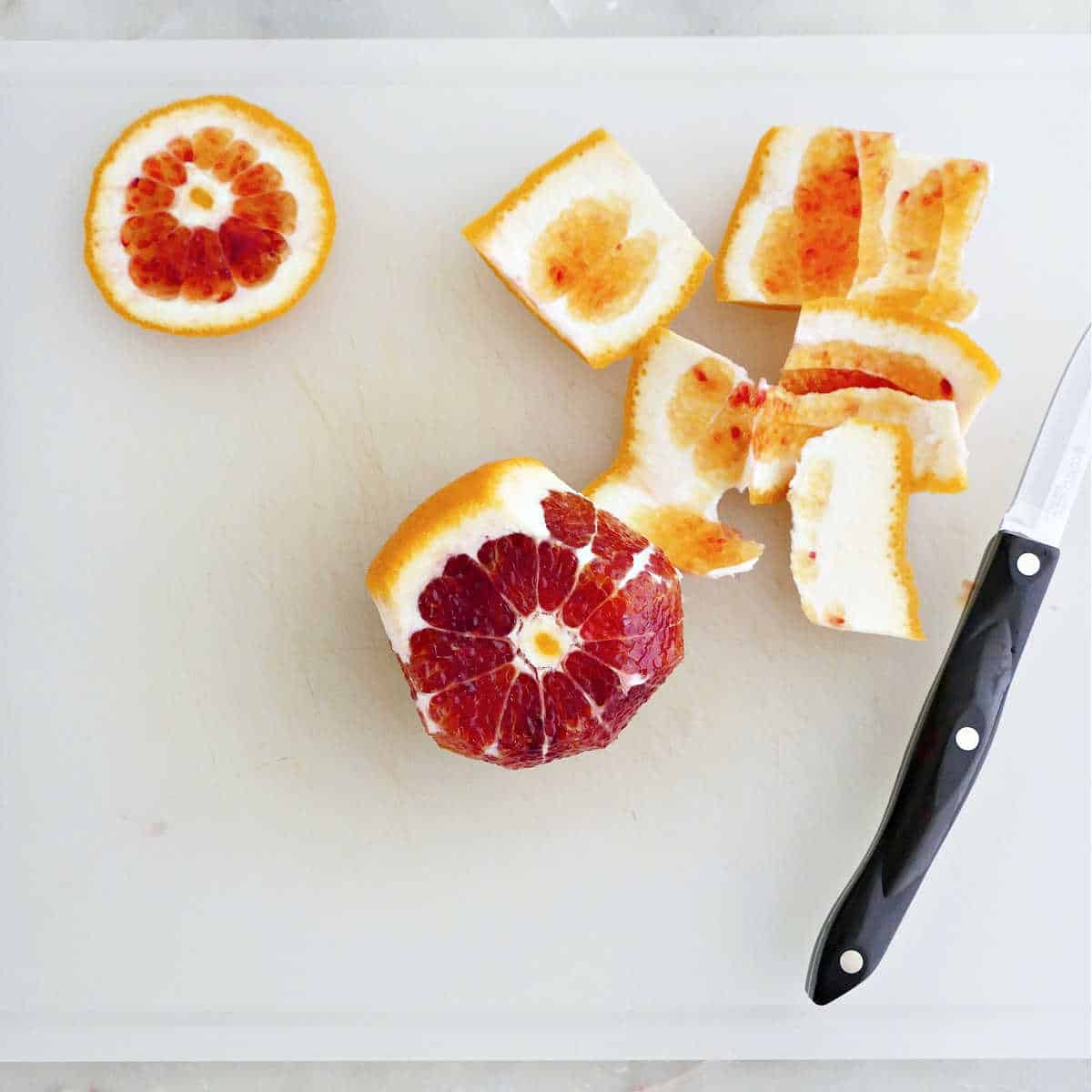 Blood orange skin cut off with a paring knife on a cutting board.