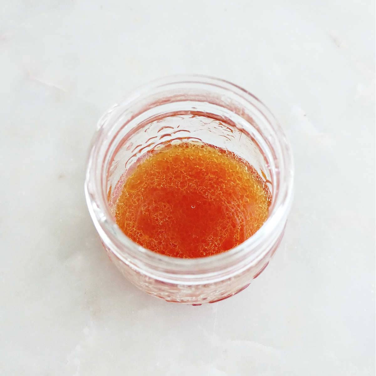 Orange juice mixed with olive oil in a small glass jar.