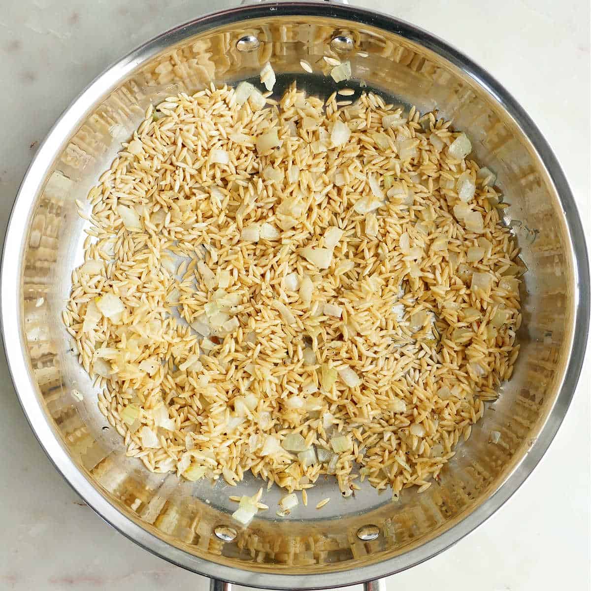 Orzo toasting in a skillet with onion and garlic.