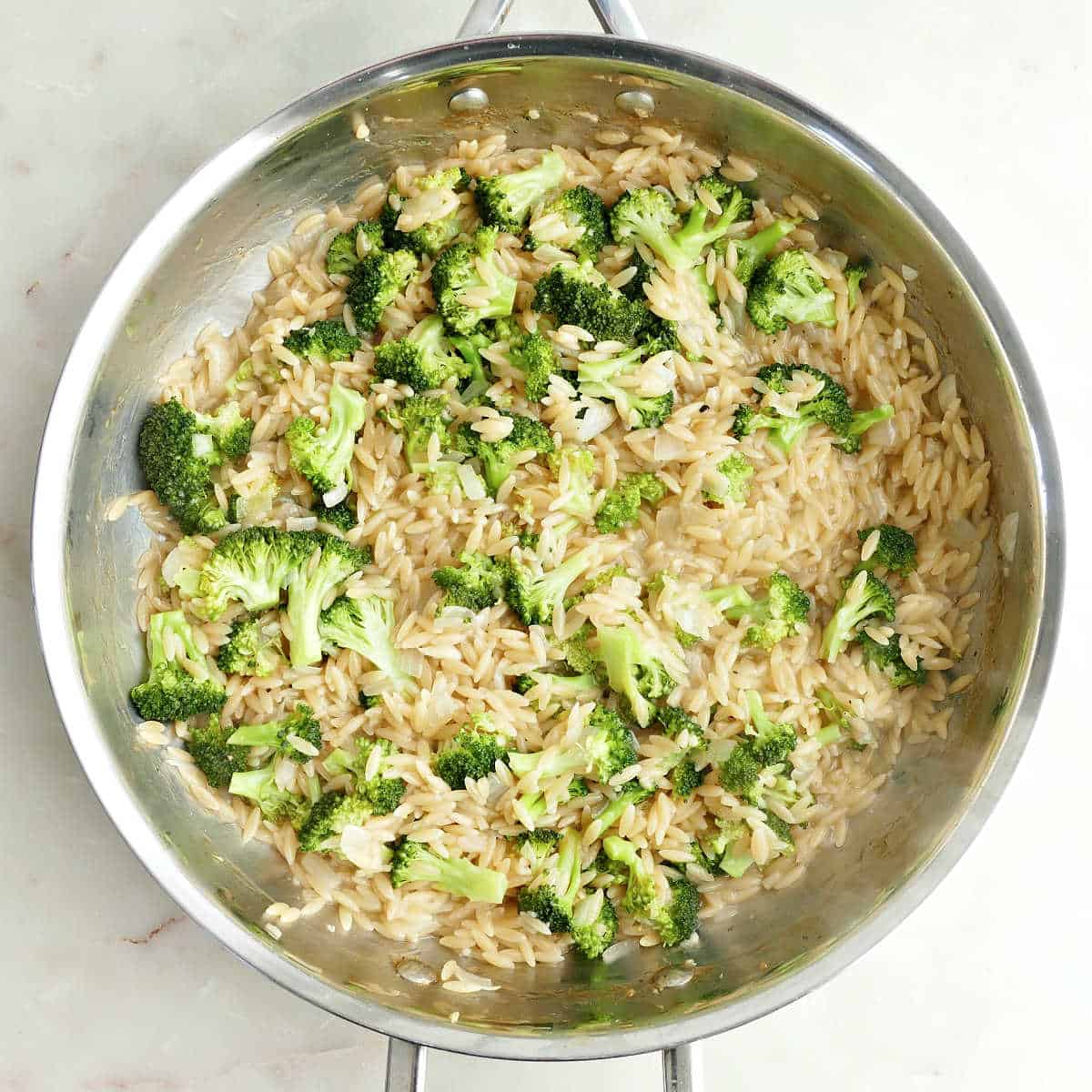 Orzo and broccoli cooked down after simmering in a skillet.