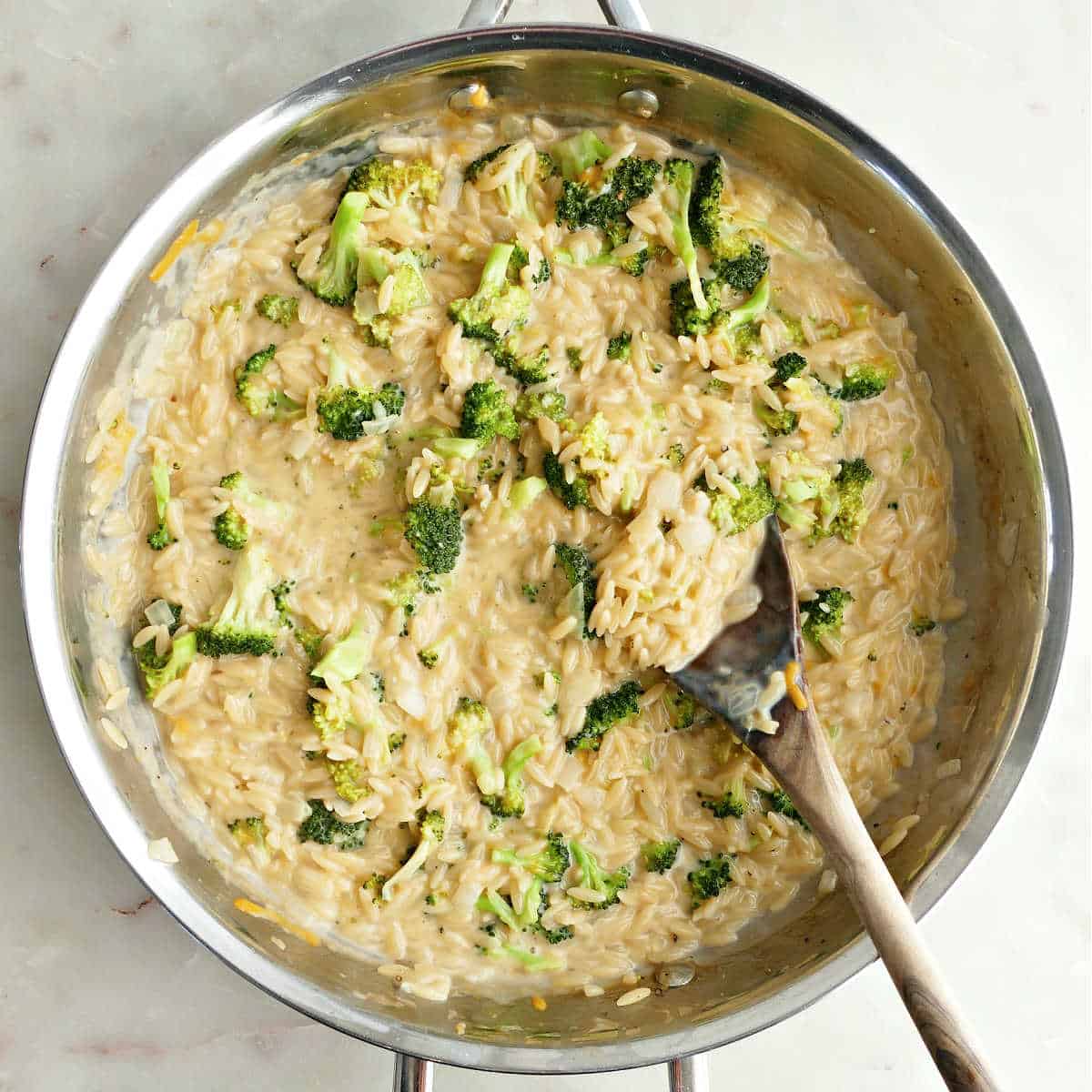 Broccoli orzo skillet after cooking with a wooden spoon.