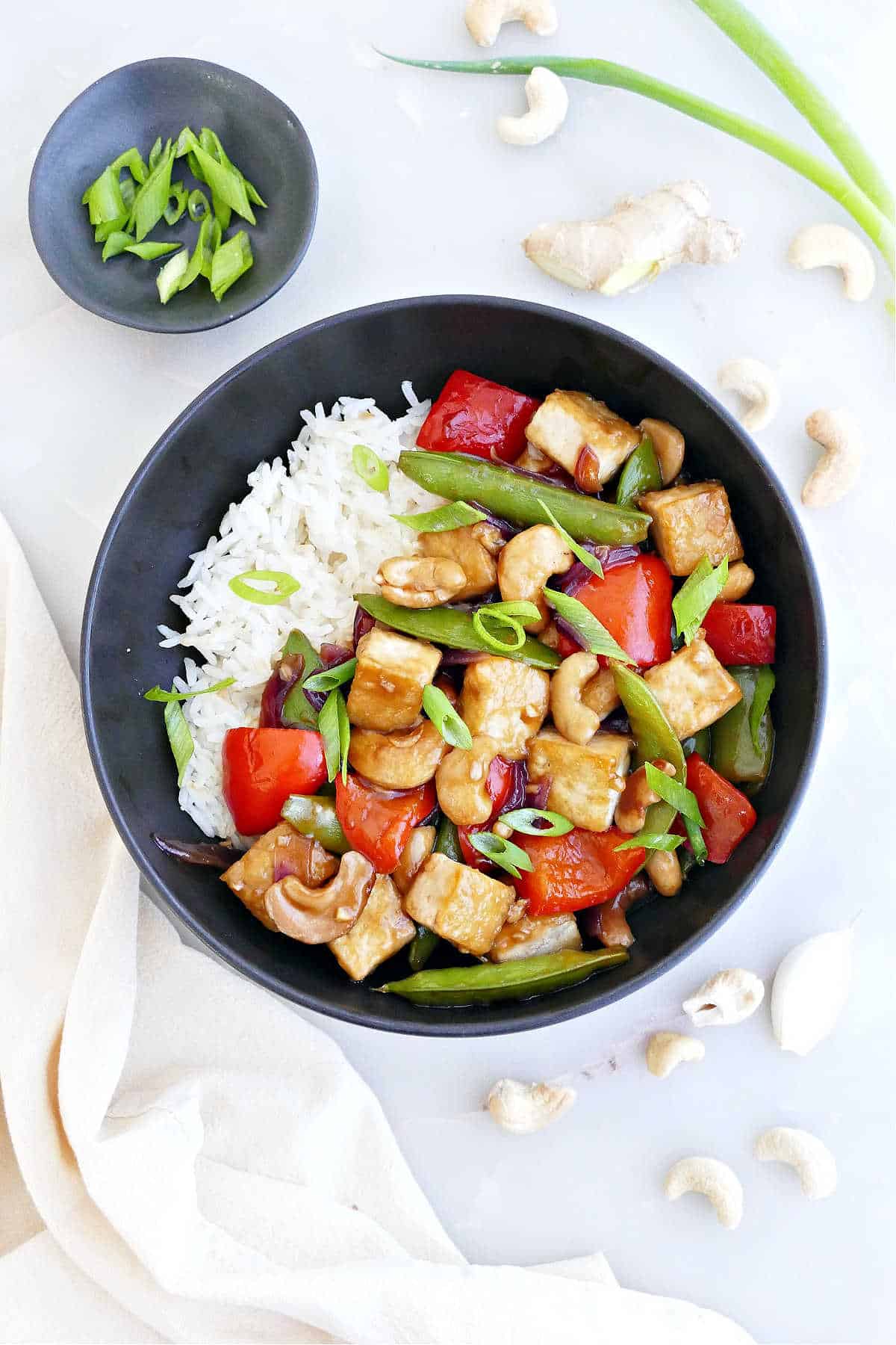 Cashew tofu stir fry with rice in a bowl next to ingredients and a napkin.