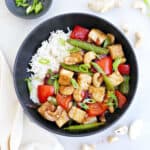 Cashew tofu stir fry with rice in a bowl next to ingredients and a napkin.
