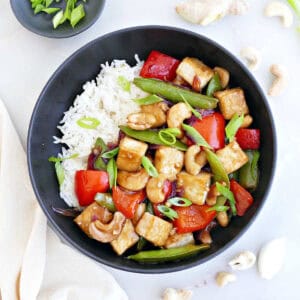 Cashew tofu stir fry with rice in a bowl next to ingredients and a napkin.