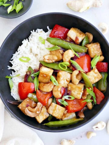 Cashew tofu stir fry with rice in a bowl next to ingredients and a napkin.