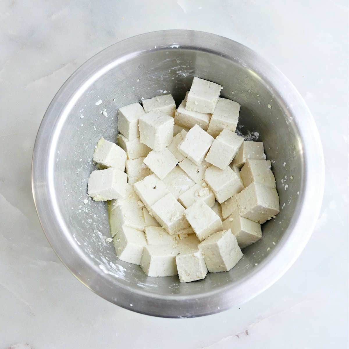 Tofu cubes being tossed in cornstarch and olive oil in a bowl.