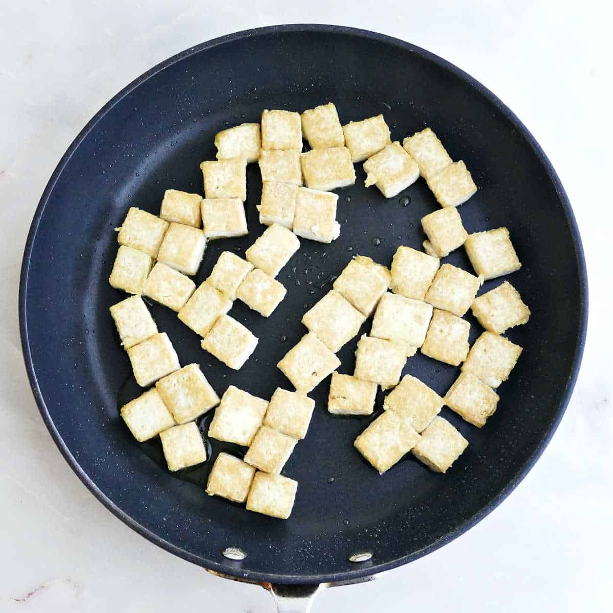 Tofu cubes cooking in a skillet until crispy.