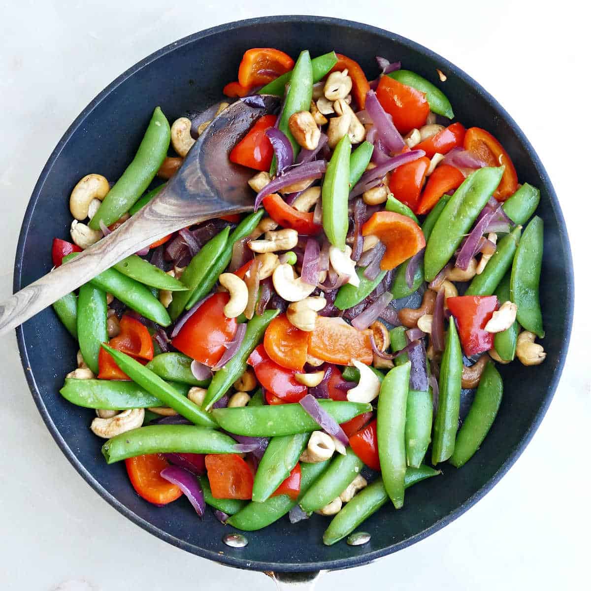 Snow peas, peppers, onions, and cashews cooking in olive oil in a skillet.