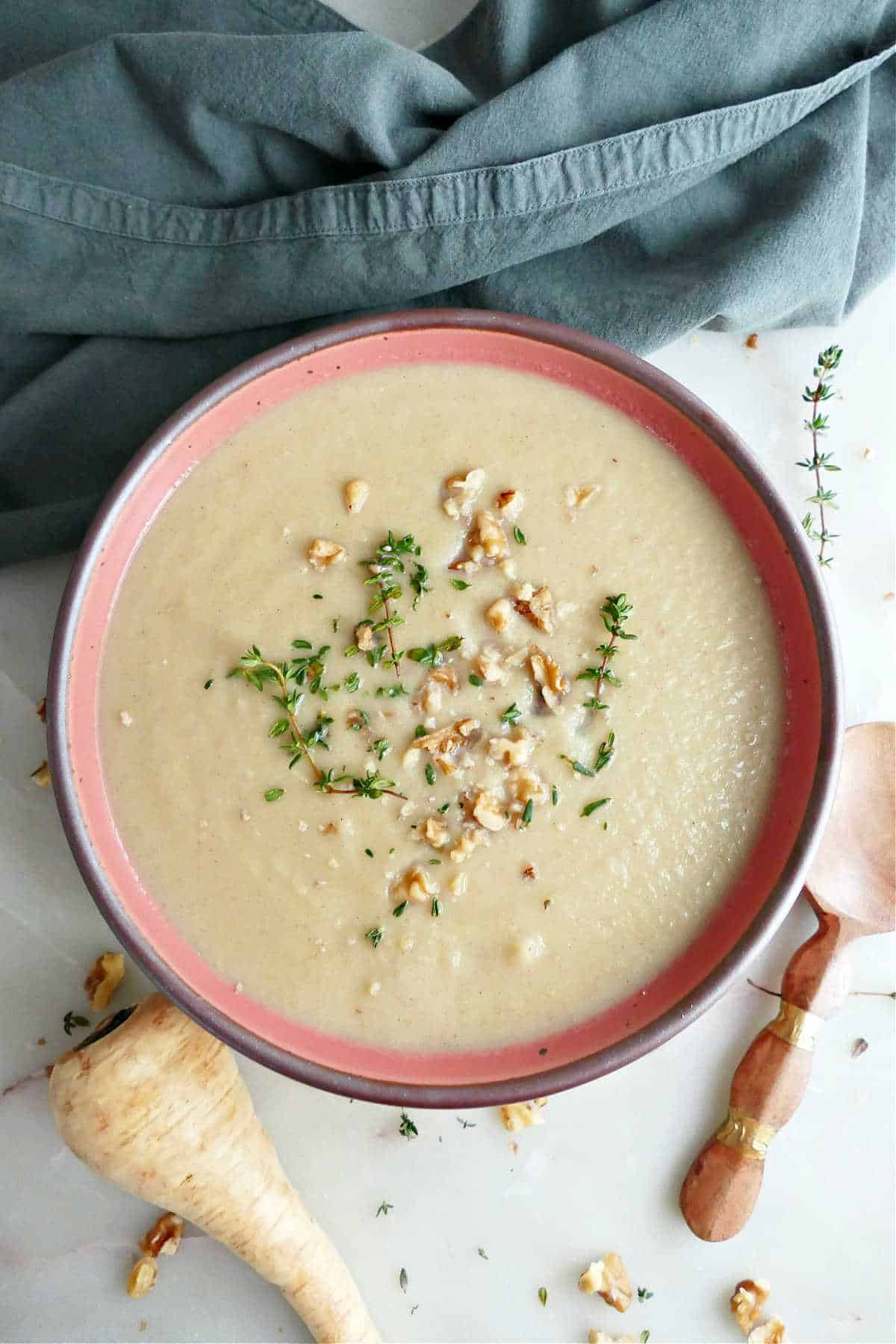 Parsnip leek soup with thyme and walnuts next to ingredients, garnishes, spoon, and napkin.