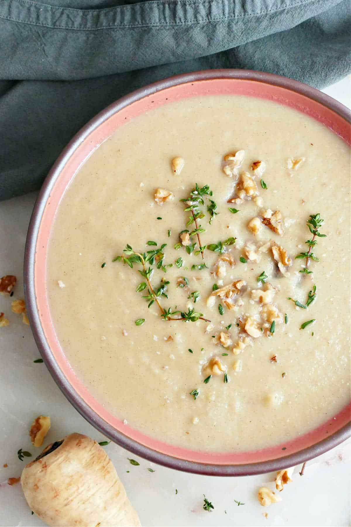 Creamy parsnip and leek soup in a bowl with thyme and walnuts.