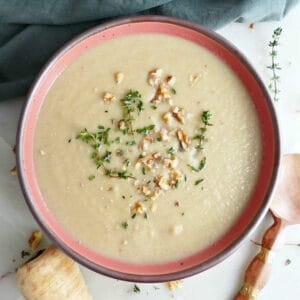 Parsnip leek soup with thyme and walnuts next to ingredients, garnishes, spoon, and napkin.