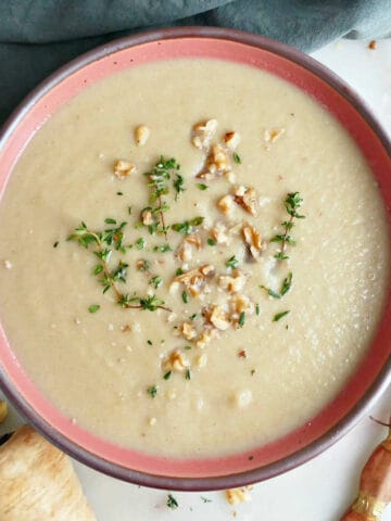 Parsnip leek soup with thyme and walnuts next to ingredients, garnishes, spoon, and napkin.