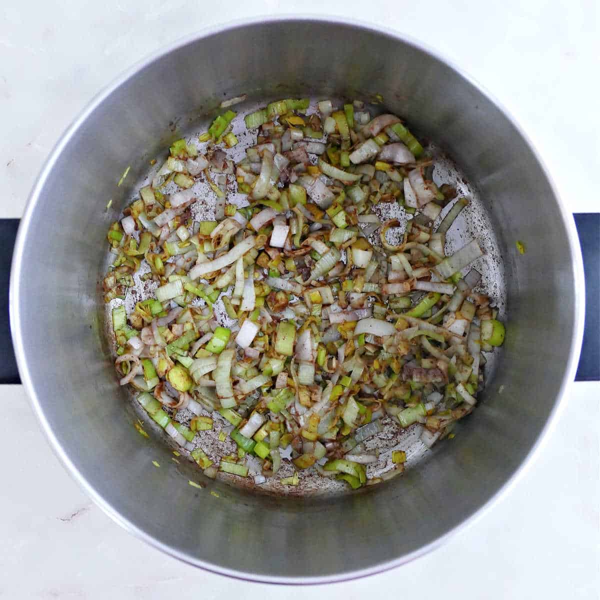 Leeks cooking in olive oil with spices in a soup pot.