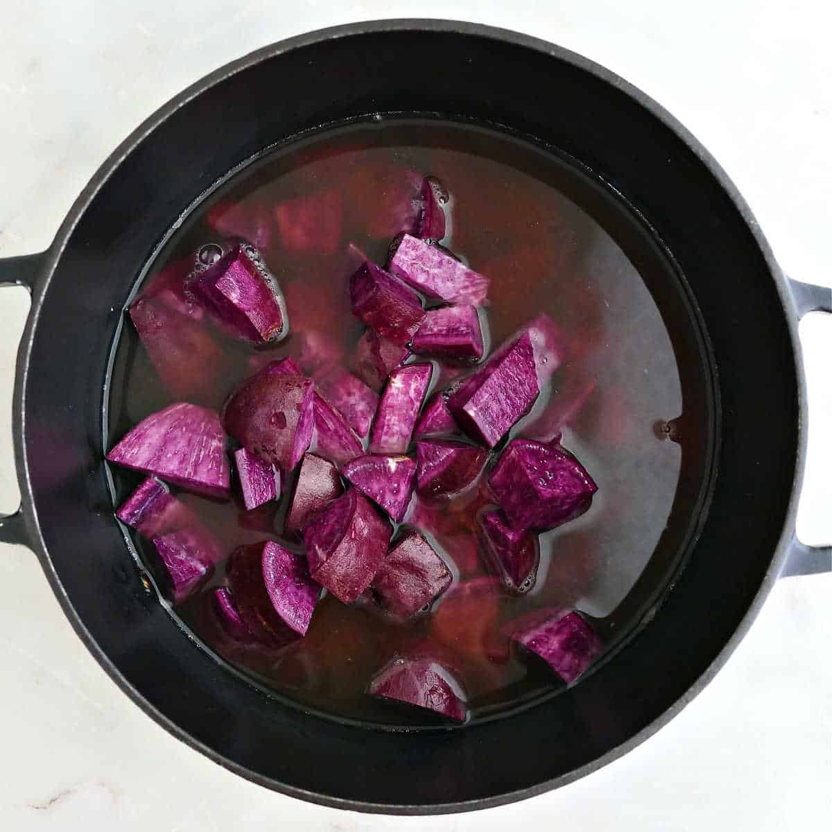 Purple sweet potatoes and broth added to a soup pot.