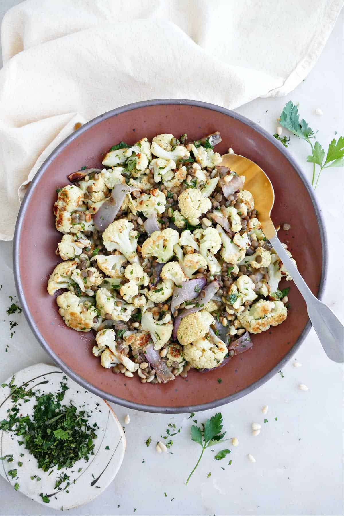 Cauliflower and lentil salad in a bowl with a spoon next to herbs and napkin.
