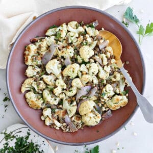Cauliflower and lentil salad in a bowl with a spoon next to herbs and napkin.