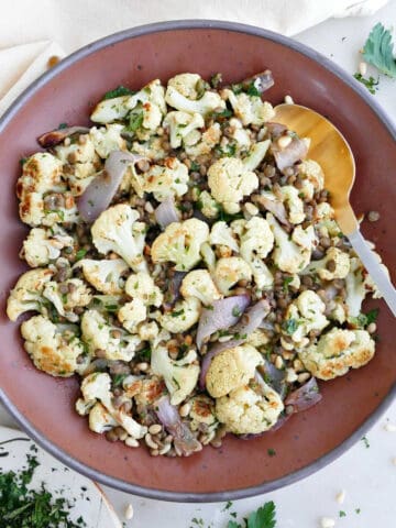 Cauliflower and lentil salad in a bowl with a spoon next to herbs and napkin.