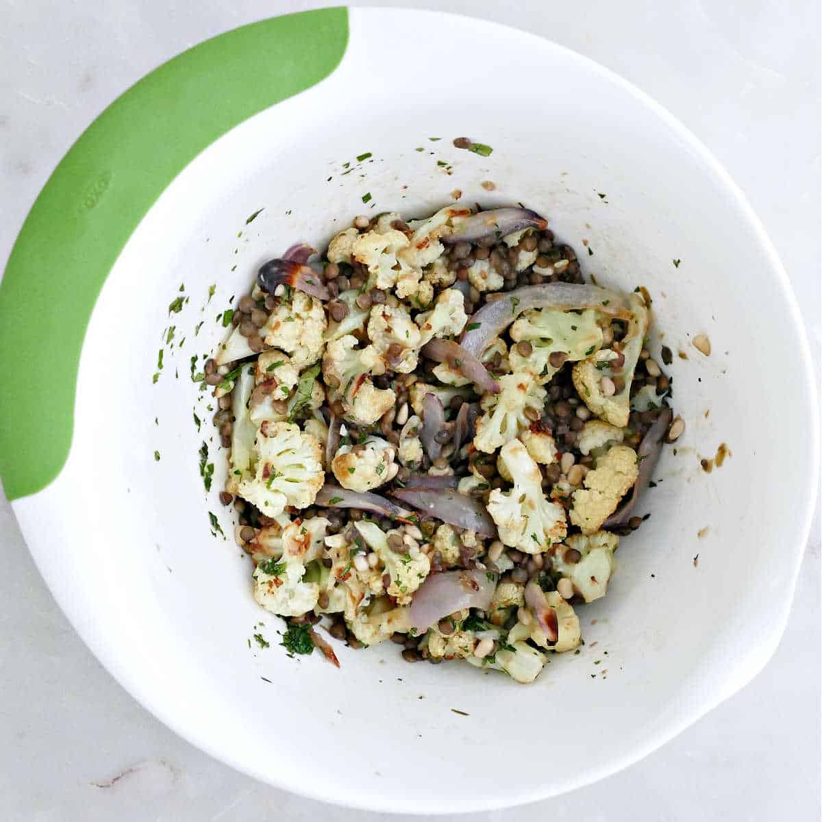 Cauliflower and lentil salad tossed in dressing in a mixing bowl.