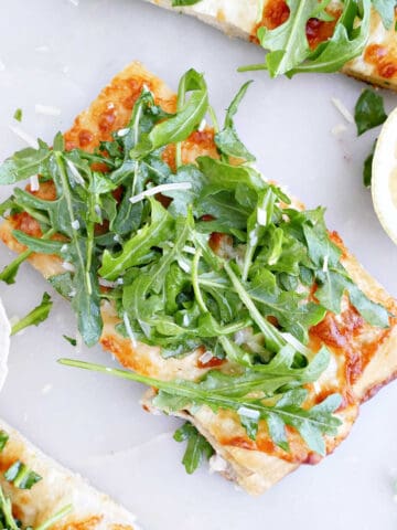 Slice of white pizza topped with arugula pizza next to other pieces and a lemon.